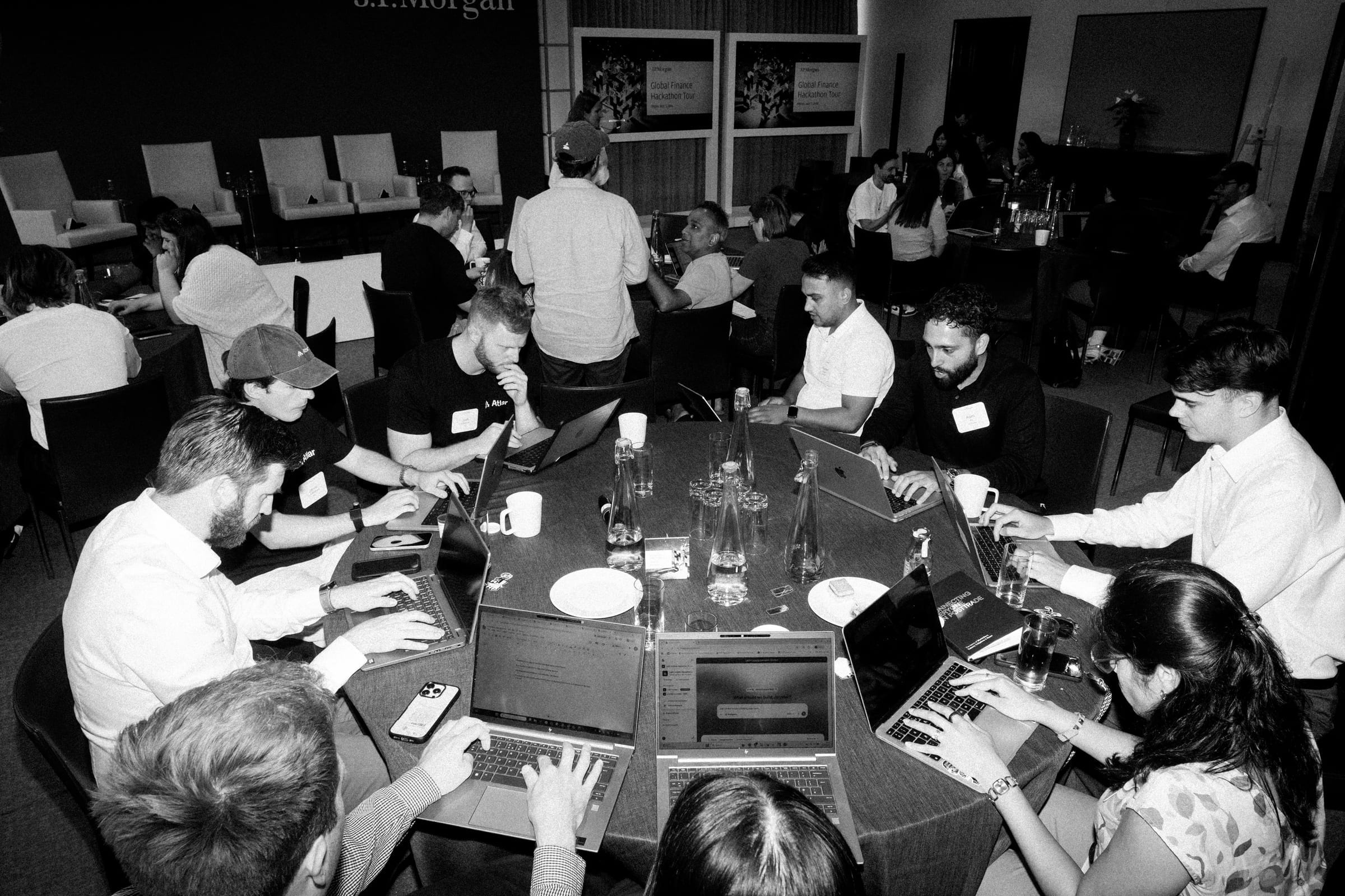 Finance leaders working together at the London hackathon, with the J.P. Morgan Global Finance Hackathon Tour banner behind them
