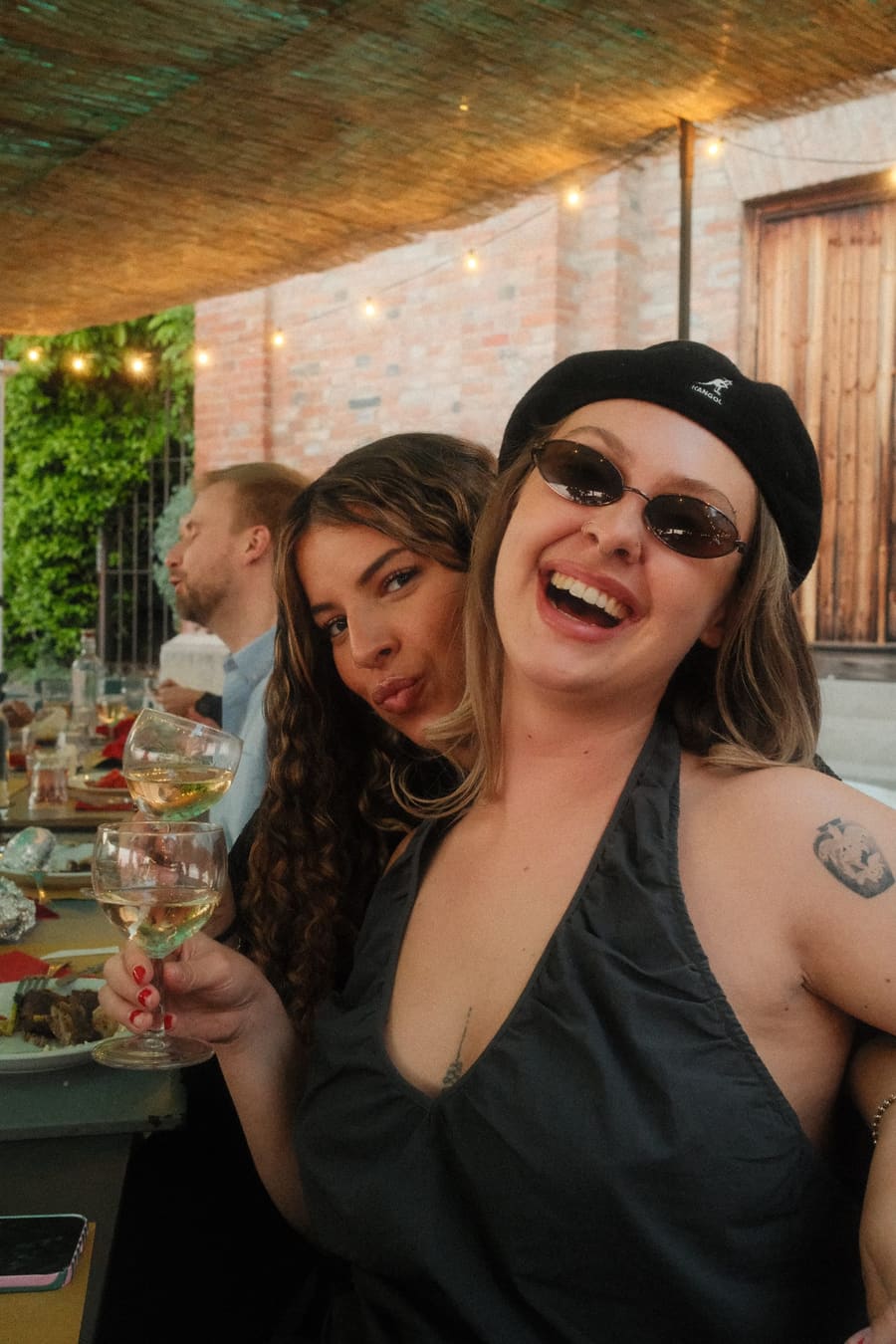 Two teammates laughing at an outdoor dinner, one raising a glass of wine