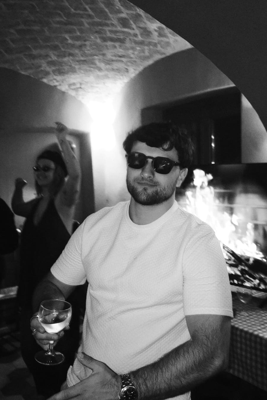 A teammate holding a drink beside a crackling outdoor fireplace at night