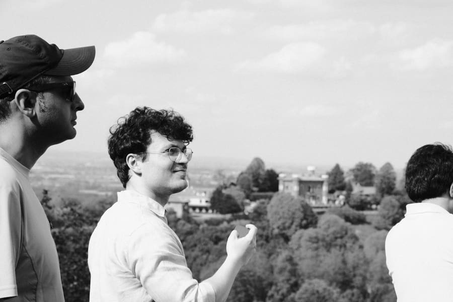 A teammate gesturing mid-conversation with two colleagues, a countryside villa in the distance
