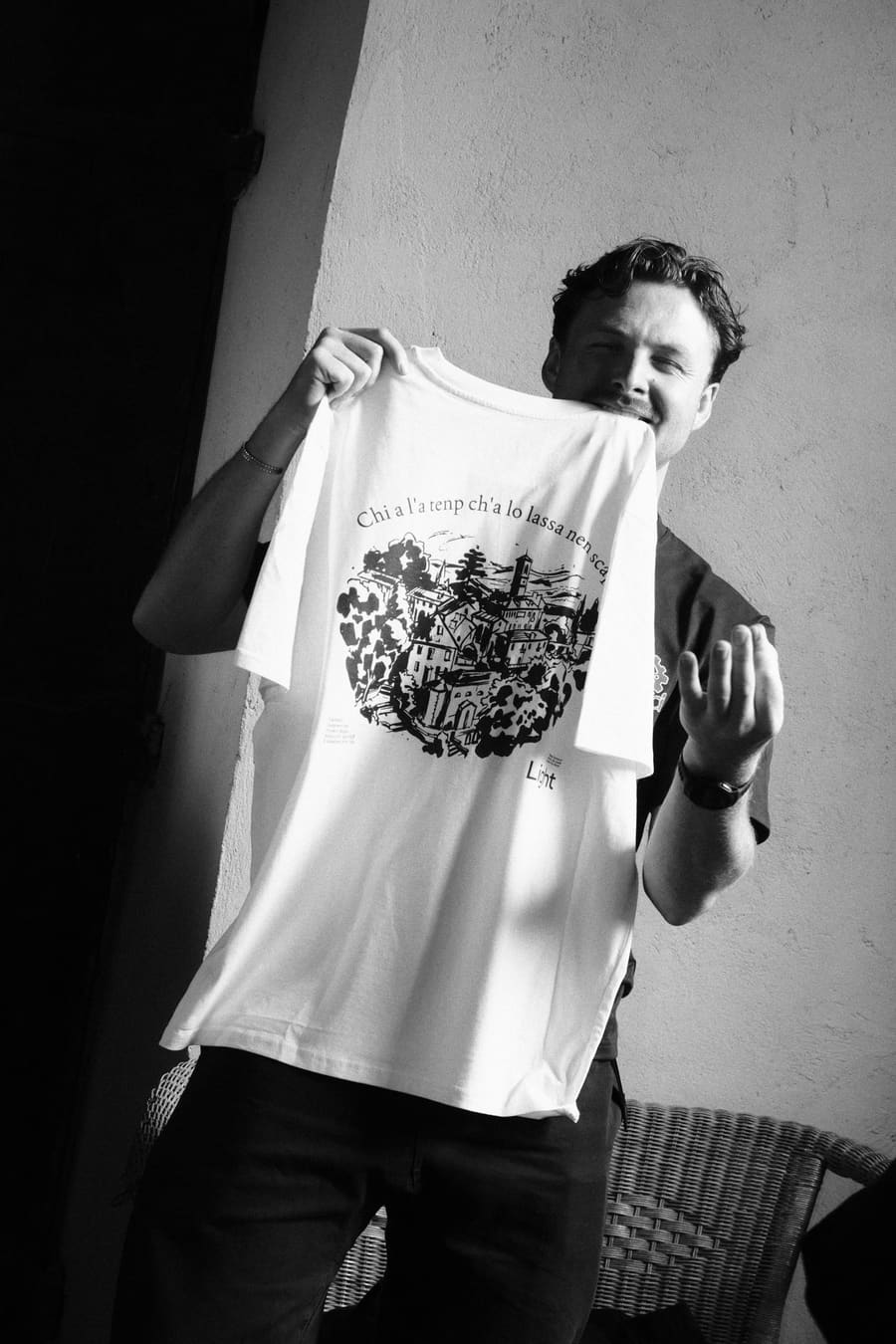 A teammate holding up a Light t-shirt printed with an illustrated village