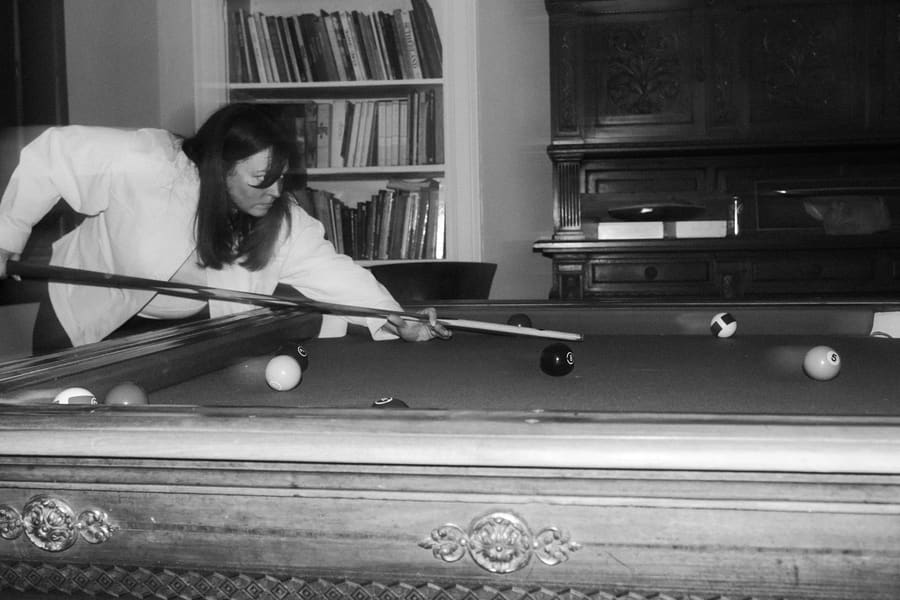 A teammate lining up a shot at a pool table in a book-lined room