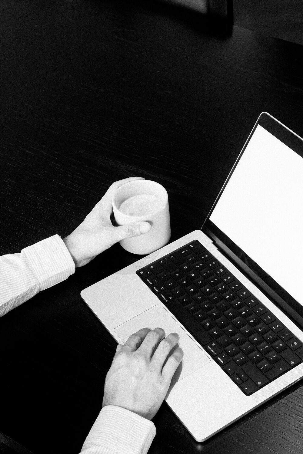 Hands with a coffee cup beside a laptop
