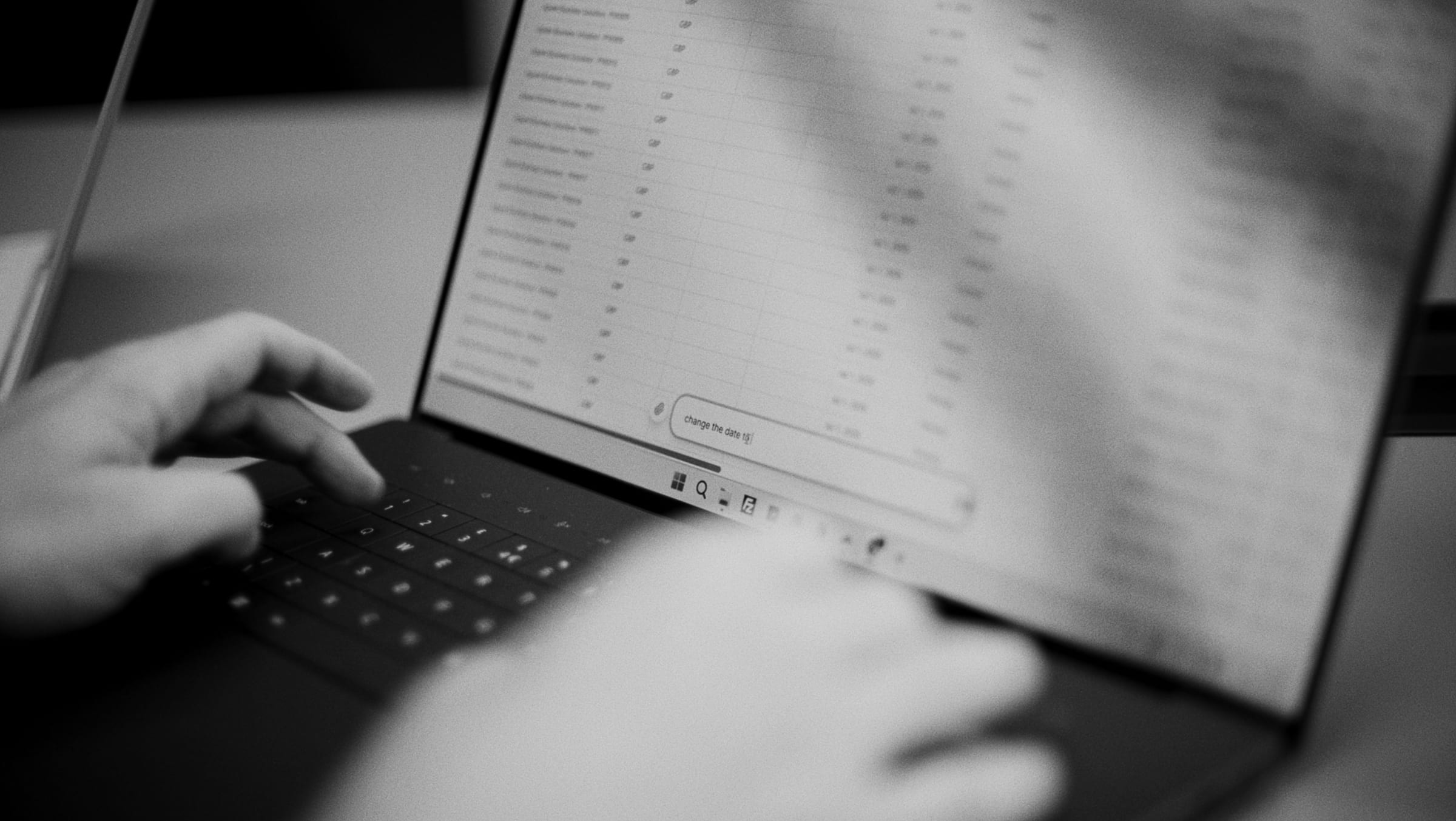 Typing on a laptop while reviewing a ledger of transactions